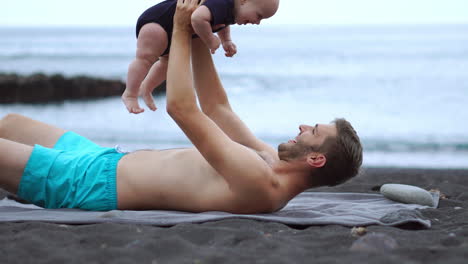 Enjoying-the-beach,-a-young-father-playfully-interacts-with-his-newborn-son.-Creating-cherished-memories,-he-embraces-his-vacation-wholeheartedly.-He's-a-dad-full-of-happiness